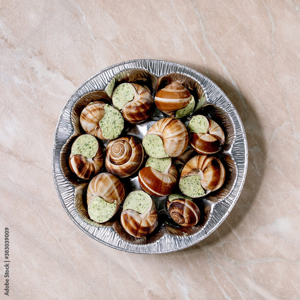 Frozen Uncooked Escargots de Bourgogne - Snails with herbs butter, gourmet dish, in store aluminum packaging over pink marble background. Flat lay, space