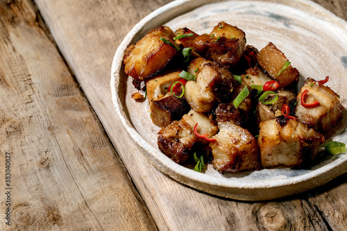 Grilled deep fried pork belly with chili pepper and spring onion on ceramic plate with chopsticks over old wooden background. Flat lay, copy space