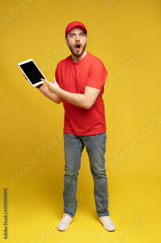 Happy delivery man with tablet in studio isolated yellow background