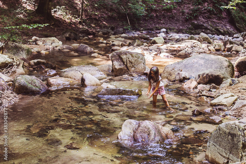 Happy little girl have fun in clear mountain rocky creek at summer forest. Beautiful natural day light. Adventure
