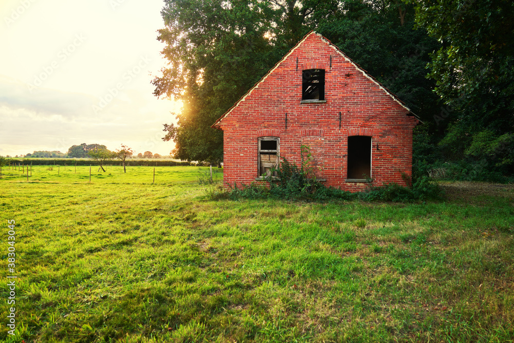 abandoned damaged shed made of red bricks on a green meadow against evening sky abandoned damaged shed made of red bricks on a green meadow against evening sky