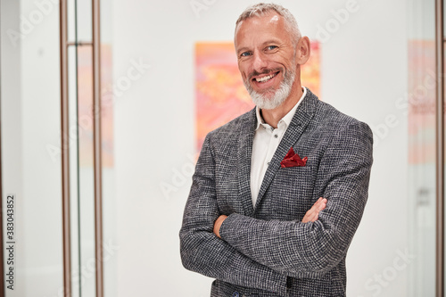 Smiley grey-haired man in a fancy blazer posing indoors