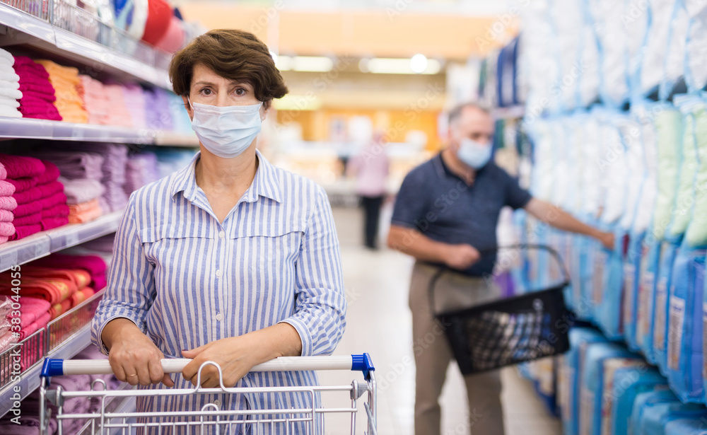 Woman in protective mask choosing bathroom towel in supermarket