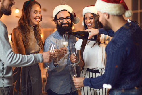 Young man pouring champagne into his friends' glasses at Christmas or New Year Party