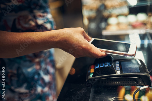 Cuadro en lienzo Woman paying in coffee shop using contactless method of payment via mobile phone
