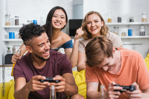 KYIV, UKRAINE - JULY 28, 2020: selective focus of excited asian woman showing winner gesture near multicultural friends playing video game