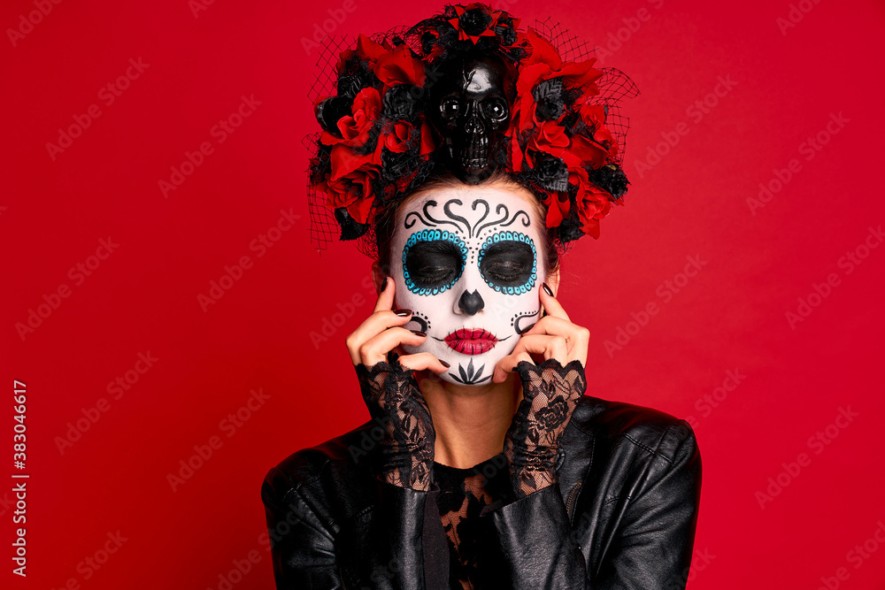Young creepy lady calavera. wears artistic make-up for the feast of all the dead. dressed in a black leather jacket with a wreath of flowers on her head.Symbol of the Day of the Dead isolated in red. Young creepy lady calavera. wears artistic make-up for the feast of all the dead. dressed in a black leather jacket with a wreath of flowers on her head.Symbol of the Day of the Dead isolated in red.