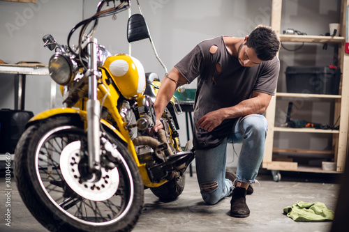 A modern young man in a t-shirt and jeans is engaged in bike diagnostics in a repair shop or garage