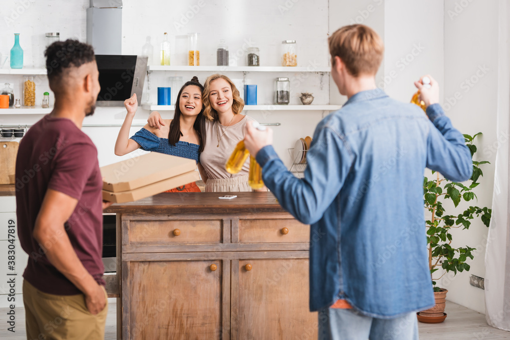 Fototapeta premium back view of multicultural friends holding pizza boxes and beer near women showing yeah gesture