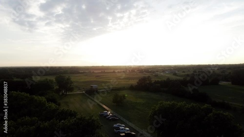 Aerial over cars parked on hilly Kansas farmland and towards the sun at sunset photo