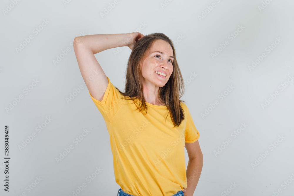 Young woman in yellow t-shirt, shorts thinking with hand on head and looking cheerful , front view. Young woman in yellow t-shirt, shorts thinking with hand on head and looking cheerful , front view.