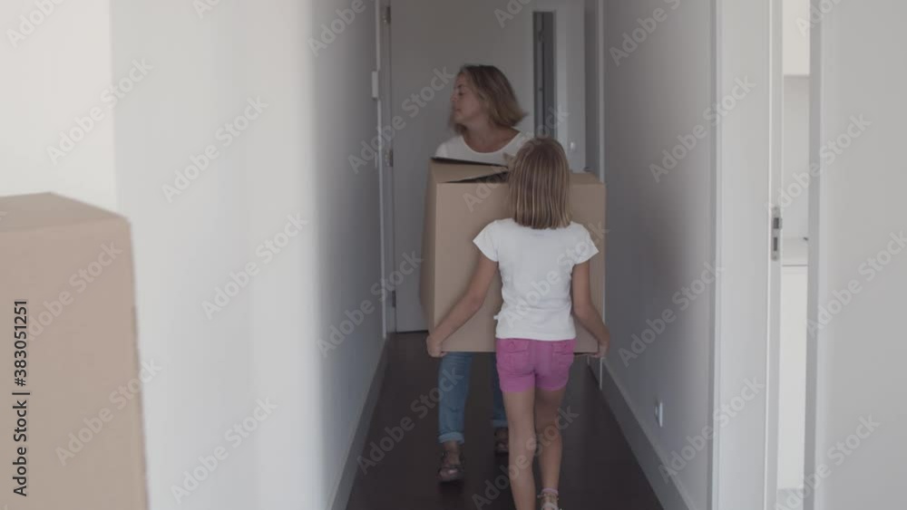 Mom and daughter carrying cartoon box to entrance Family leaving apartment. Dolly shot. Relocation concept Mom and daughter carrying cartoon box to entrance Family leaving apartment. Dolly shot. Relocation concept