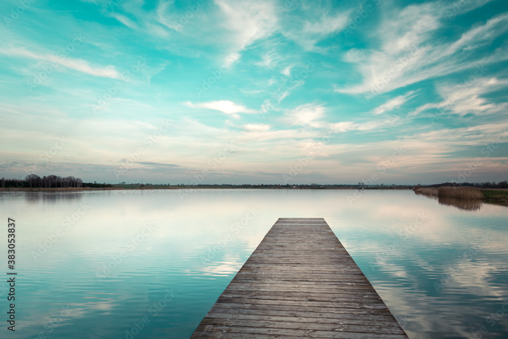 A wooden jetty towards water and clouds against a blue sky