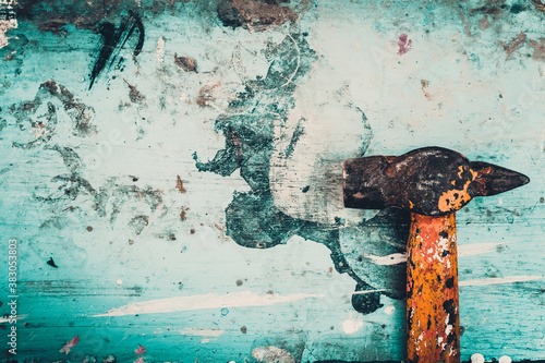 The background is splattered with paint. An old hammer on a stained wooden surface