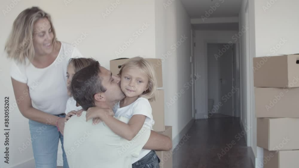 Two girls running to dad and hugging him among carton boxes in their new apartment. Moving into new house concept Two girls running to dad and hugging him among carton boxes in their new apartment. Moving into new house concept