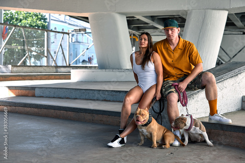 young stylishly dressed man and woman with an athletic figure with two american bully dogs under the bridge on city streets