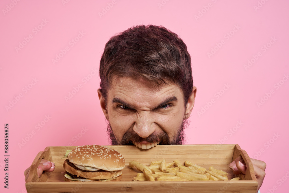 Aggressive guy with a tray in his hands hamburger fries pink background hungry look Aggressive guy with a tray in his hands hamburger fries pink background hungry look