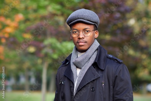 Portrait of handsome stylish young black African Afro American man in coat, scarf, hat and glasses looking at camera, walking in golden autumn park  © Евгений Шемякин