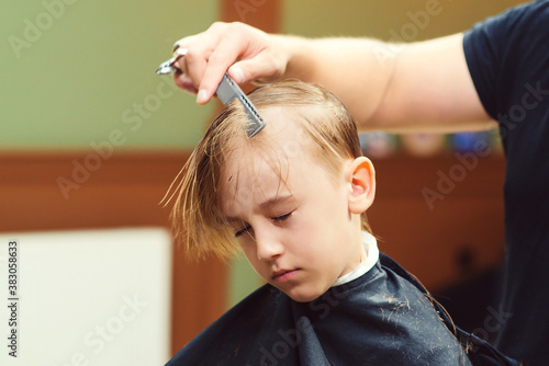 Cute little boy getting haircut by hairdresser at the barbershop. New hairstyle for young boy.