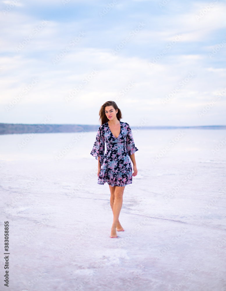 beautiful girl with brown hair in a black dress with a color pattern walks on a salty pink still water lake at a vanilla sunset beautiful girl with brown hair in a black dress with a color pattern walks on a salty pink still water lake at a vanilla sunset