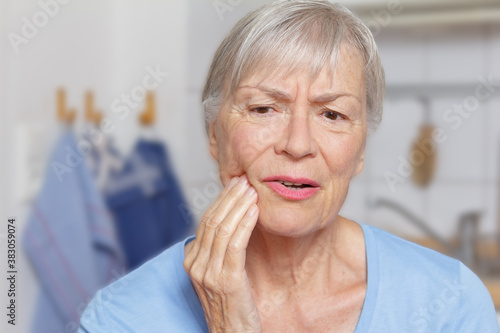 Billede på lærred Acute toothache: senior woman in her kitchen with a hand at her painful jaw