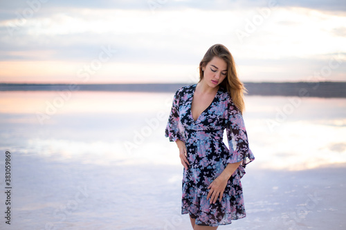 beautiful girl with brown hair and big eyes in a black dress with a colored pattern on a salty pink lake at a vanilla sunset