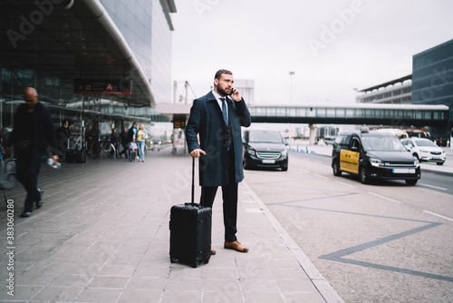Caucasian businessman using mobile phone for calling after arrival to airport terminal, male lawyer with baggager using cellphone application for contact customer service and order cab taxi