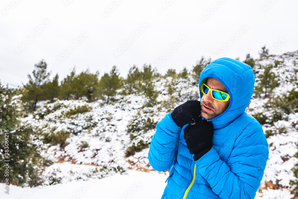 Mountaineer man with blue coat and sunglasses walking on a snowy mountain path in his spare time.