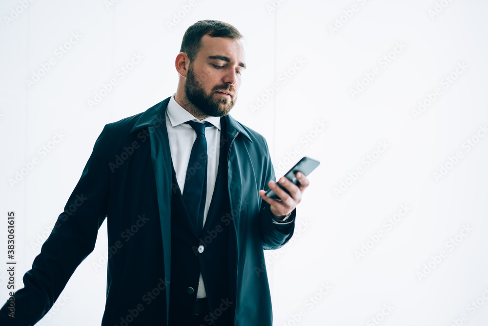 Formally dressed male entrepreneur using cellular application for checking account balance near publicity area, Caucasian businessman messaging via smartphone near mockup backdrop with copy space area Formally dressed male entrepreneur using cellular application for checking account balance near publicity area, Caucasian businessman messaging via smartphone near mockup backdrop with copy space area