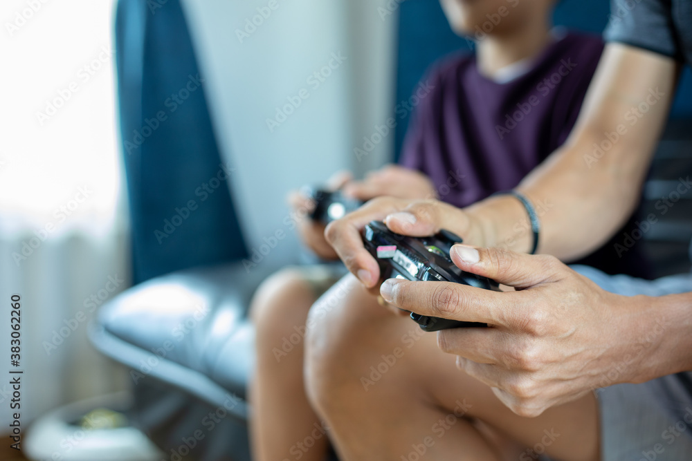 Fototapeta premium Asian father and son enjoy playing video games together with video joystick with excite and very fun in the living room at home