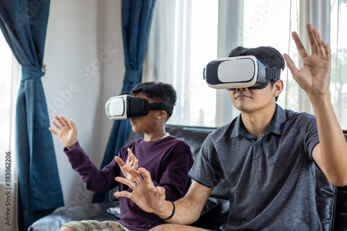 Asian father and son enjoy playing video games together with video joystick and Virtual Reality Glasses with exciting and very fun in the living room at home