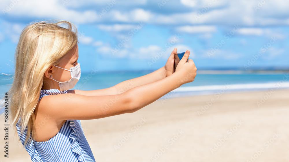 Funny girl taking selfie photo by smartphone on tropical sea beach. New rules to wear cloth face covering mask at public places due coronavirus COVID 19. Family holidays with children, summer travel. Funny girl taking selfie photo by smartphone on tropical sea beach. New rules to wear cloth face covering mask at public places due coronavirus COVID 19. Family holidays with children, summer travel.