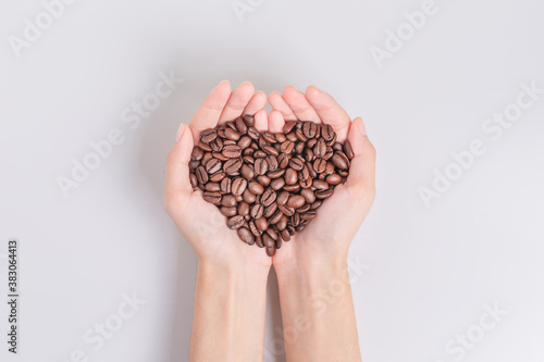 Coffee beans roasted in the hands of woman in heart shape. on white background. Top view.