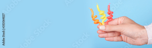 Hand with colored birthday candles. Isolated on blue background, copy space template, banner.