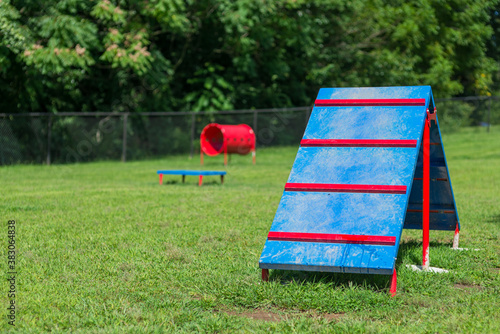 Dog agility equipment at outdoor park.  Brightly colored dog playground, with a-frame ramp, tube, and platform.  Great for exercising dogs, and training for special agility events.