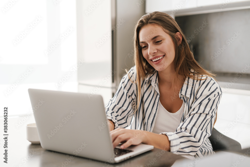 Fototapeta premium Young caucasian woman smiling while working on laptop at home