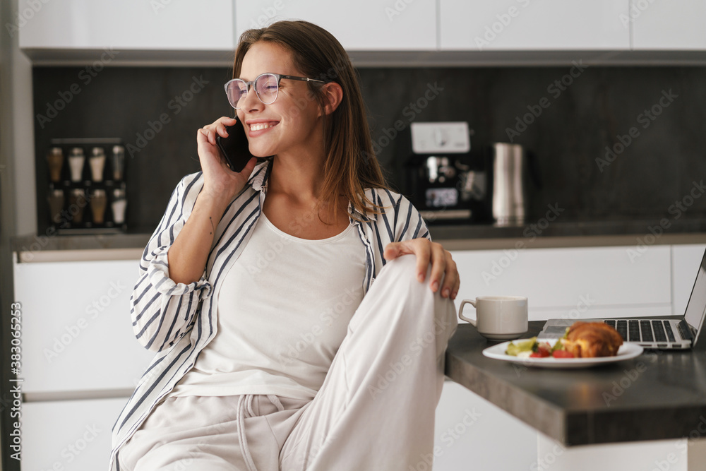 Young woman talking on cellphone while having breakfast at home
