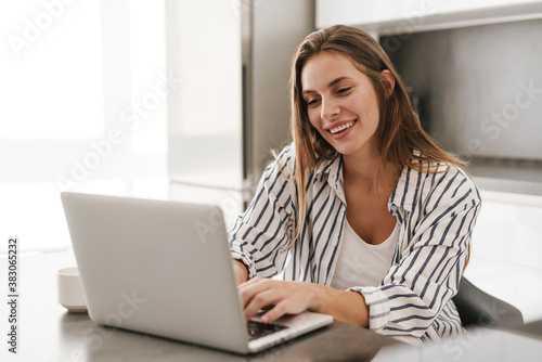Young caucasian woman smiling while working on laptop at home © Drobot Dean