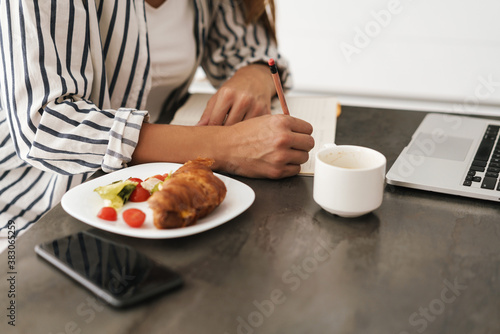Young woman writing in notebook while having breakfast at home