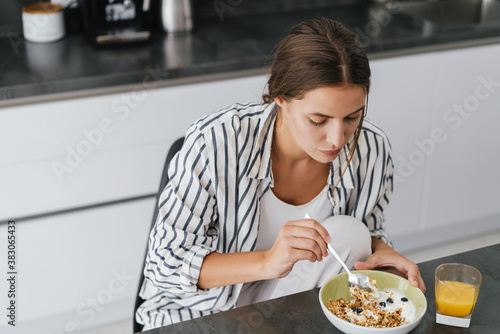 Young caucasian woman holding cellphone while having breakfast at home