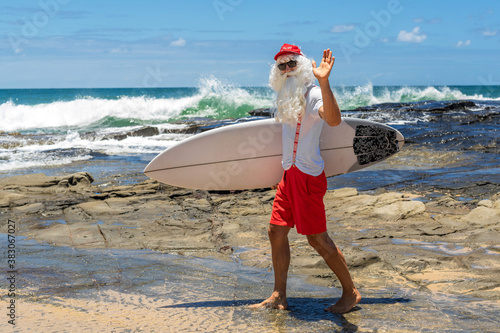 Photography Santa Claus with a surf board with the ocean on backgraund