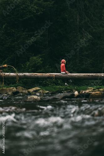 Girl in the woods is on the trunk of a fallen tree. Crossing the river.