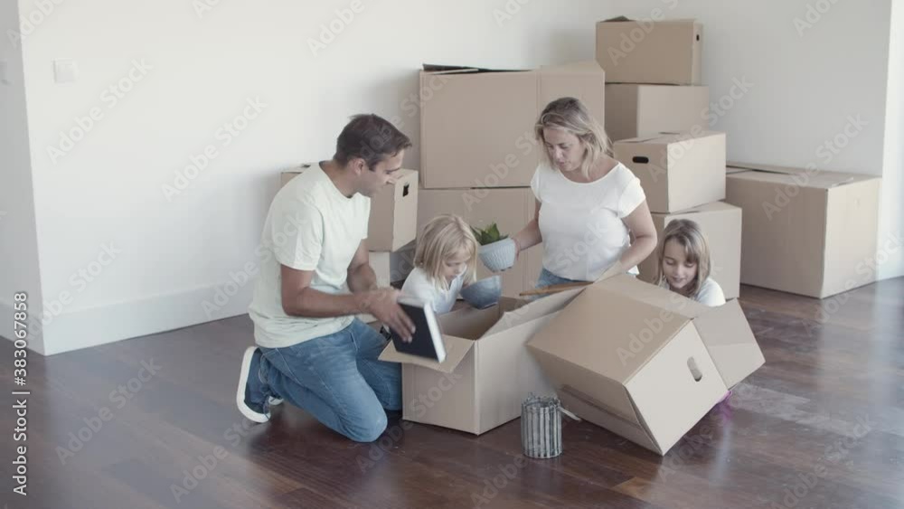Cheerful family with kids unpacking things in new apartment, sitting on floor with open boxes. Relocation or new home concept Cheerful family with kids unpacking things in new apartment, sitting on floor with open boxes. Relocation or new home concept