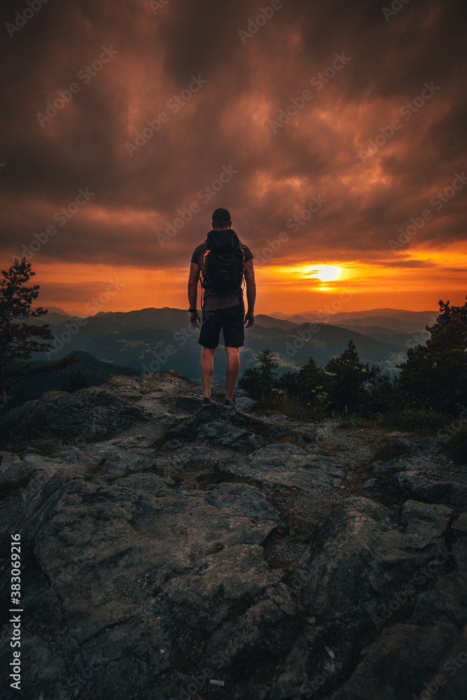 Obraz premium Hiker with backpack standing on mountain and enjoying sunset