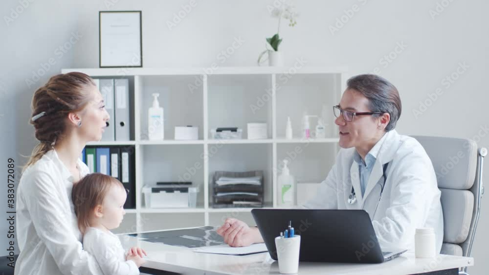 Male pediatrician is examining sick little baby. Doctor, mother and daughter in medical office in clinics. Male pediatrician is examining sick little baby. Doctor, mother and daughter in medical office in clinics.