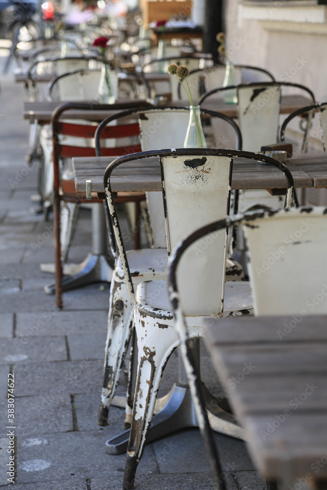 Fototapeta premium Charmantes vintage outdoor Restaurant mit verwitterten weißen Stühlen und Holztischen dekoriert mit Gläsern, Blumenvasen, Bestecken und Servietten