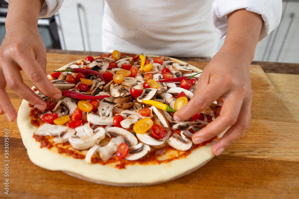 A view of the hands of the chef adding hot peppers to the pizza toppings. Vegan food.