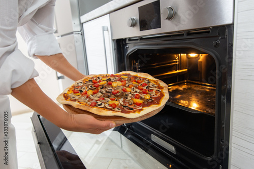 A young woman chef takes out a baked pizza from the oven on a round wooden board.