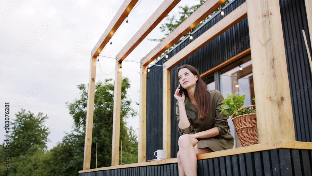 Young woman with smartphone outdoors, weekend away in container house in countryside.