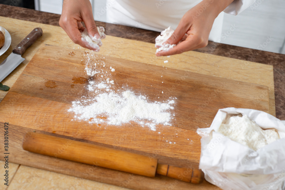 Close-up on the hands of the chef who sprinkles flour on a wooden board. Close-up on the hands of the chef who sprinkles flour on a wooden board.